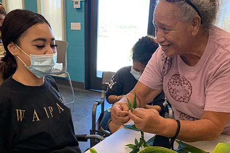 a senior teaching a teen how to make a lei